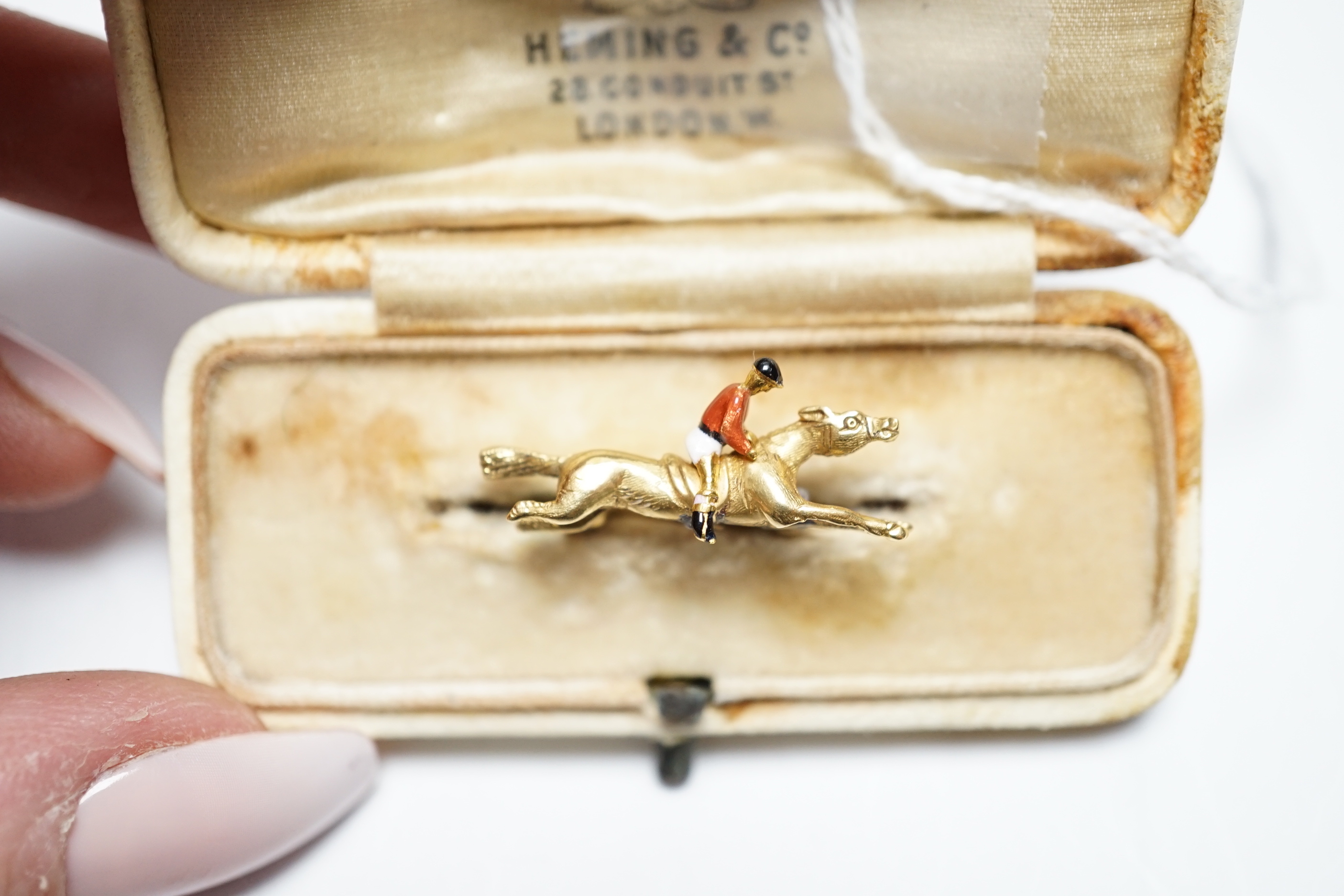 An Edwardian yellow metal, and polychrome enamelled novelty brooch, modelled as a horse with jockey, 25mm, gross weight 3,8 grams.